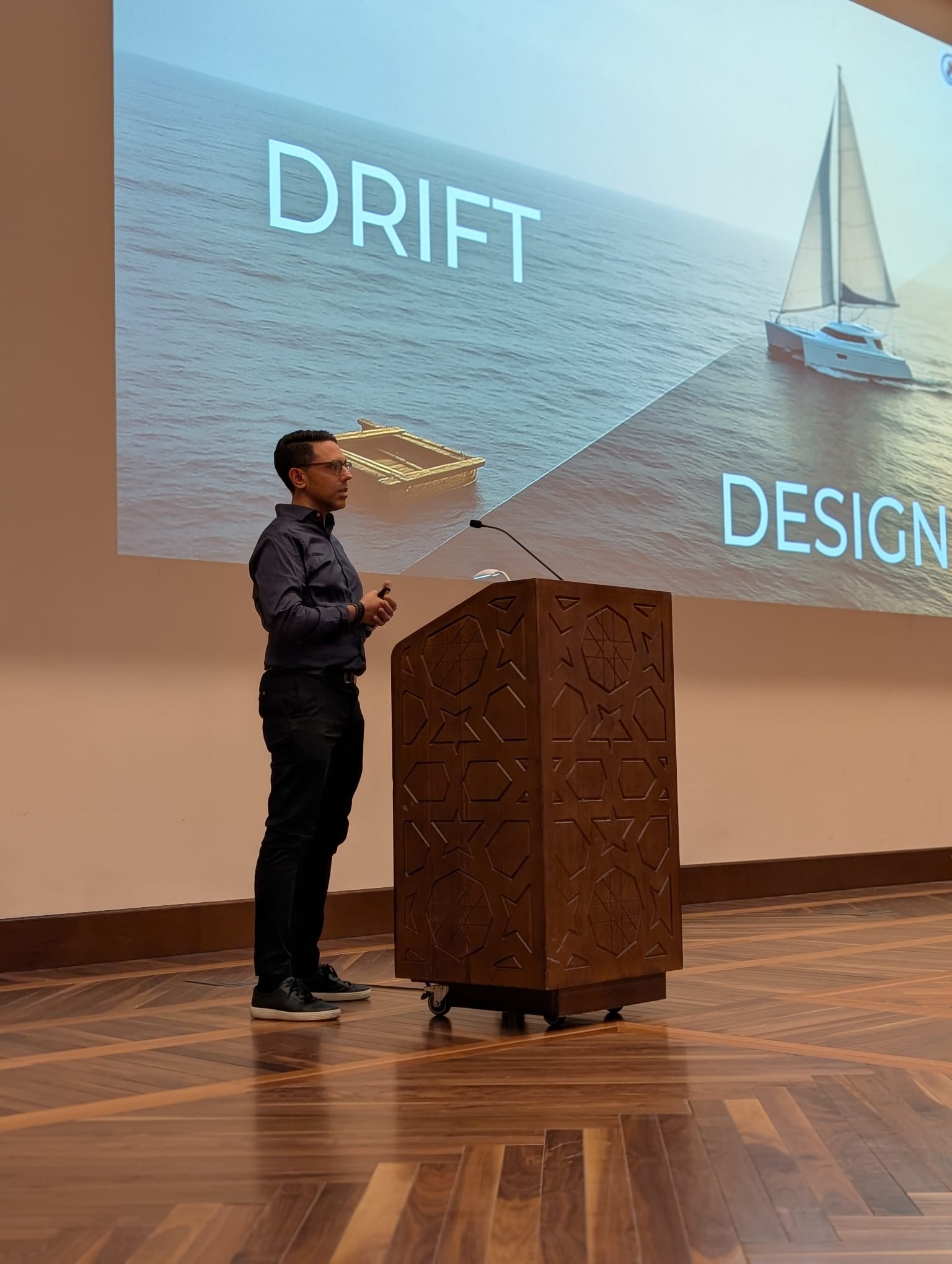 Rahim Hirji on stage, a slide behind him contrasting a drifting raft with a designed sailboat
