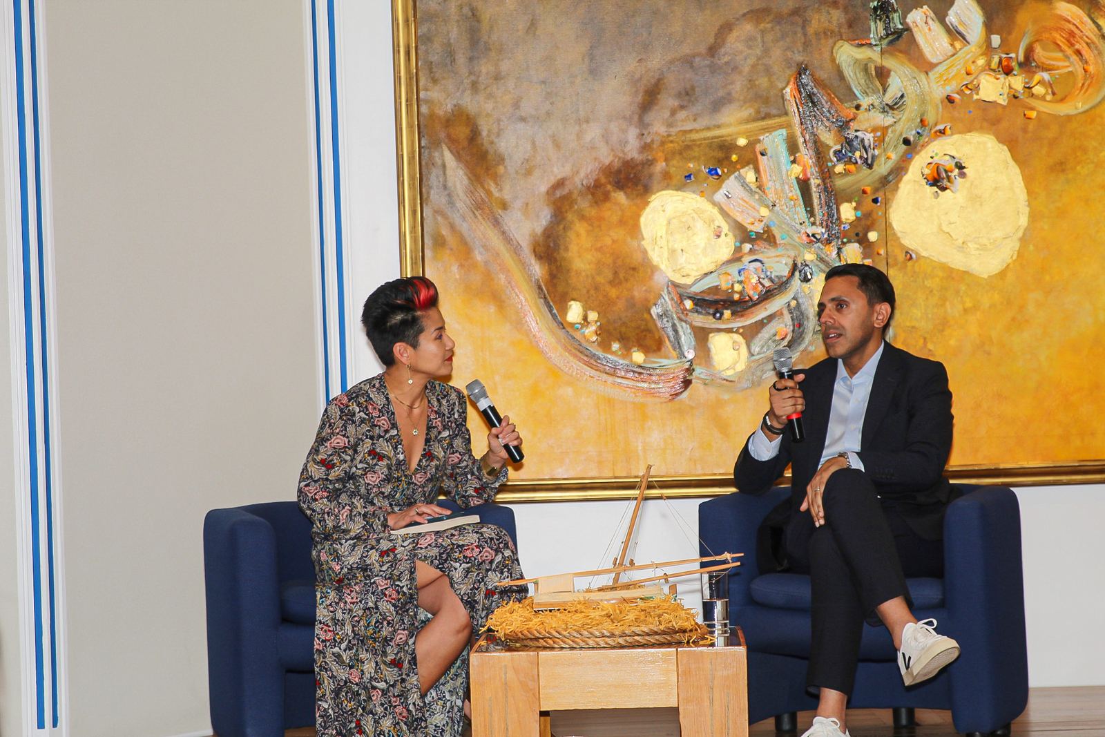 Rahim Hirji answering questions in conversation on stage at the SuperSkills launch, with the model boat on the table between the two chairs